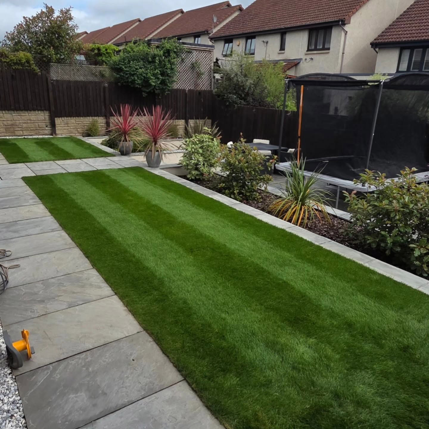 Both new lawn panels striped and green in a Kirkliston garden two weeks after turfing